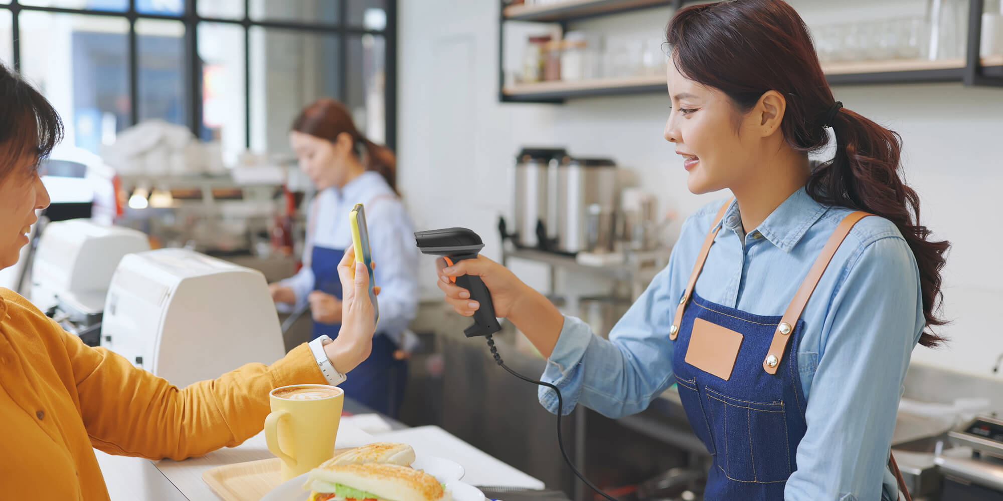 Store clerk using a handheld barcode scanner to scan a barcode from a customer’s phone Store clerk using a handheld barcode scanner to scan a barcode from a customer’s phone